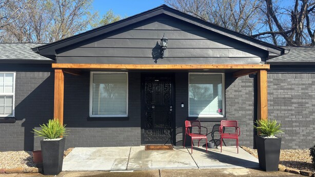A residential building with a dark gray exterior, a front porch with two red chairs, and two potted plants. - Elvis, Blues & BBQ: 4BR Home Just Outside Memphis, Minutes from USA Ball Stadium (Millington)