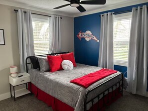 A bedroom with a bed, a nightstand, a ceiling fan, and a wall with a USA stadium mural. - Elvis, Blues & BBQ: 4BR Home Just Outside Memphis, Minutes from USA Ball Stadium (Millington)