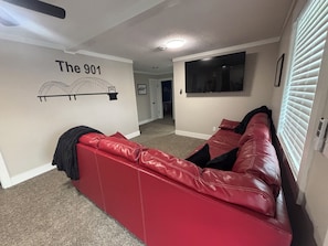 A red leather sofa in a living room with a wall mural reading "The 901" and a large window with blinds. - Elvis, Blues & BBQ: 4BR Home Just Outside Memphis, Minutes from USA Ball Stadium (Millington)