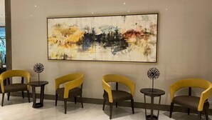A lobby with a large abstract painting, four yellow chairs, and small tables. - Skyline Suites 81 Newport Condotel NAIA T3 (Pasay City)