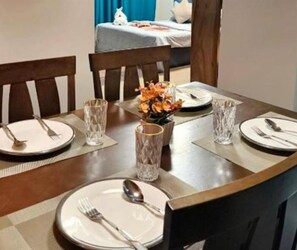 Ett matbord dukat med tallrikar, bestick och glas, och en vas med blommor i mitten.