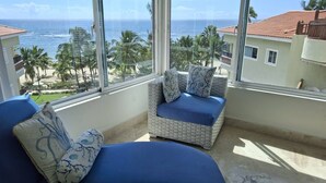 Una habitación con vista al océano, que incluye un sofá de mimbre y un sillón con cojines azules.