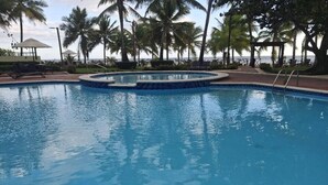 Una piscina con un jacuzzi circular, rodeada de palmeras y tumbonas, con vista al océano.