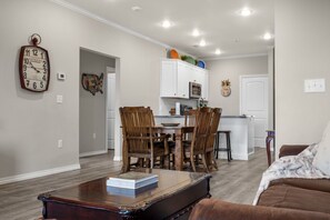 A living room with a wooden coffee table, a brown sofa, and a dining area with wooden chairs and a white cabinet. - Town-view Terrace | Pool | Minutes from 76 (Branson)
