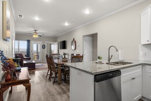 A modern kitchen with a dishwasher, a dining area with a wooden table and chairs, and a living room with a sofa and a ceiling fan. - Town-view Terrace | Pool | Minutes from 76 (Branson)