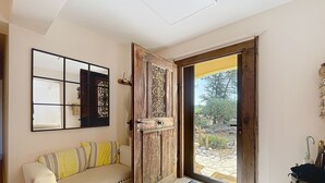 A room with a wooden door, a beige sofa with striped cushions, a wall-mounted mirror, and a metal container on the floor. - La Maison Bleue, your exceptional break in the heart of the Ardèche Gorges (Salavas)