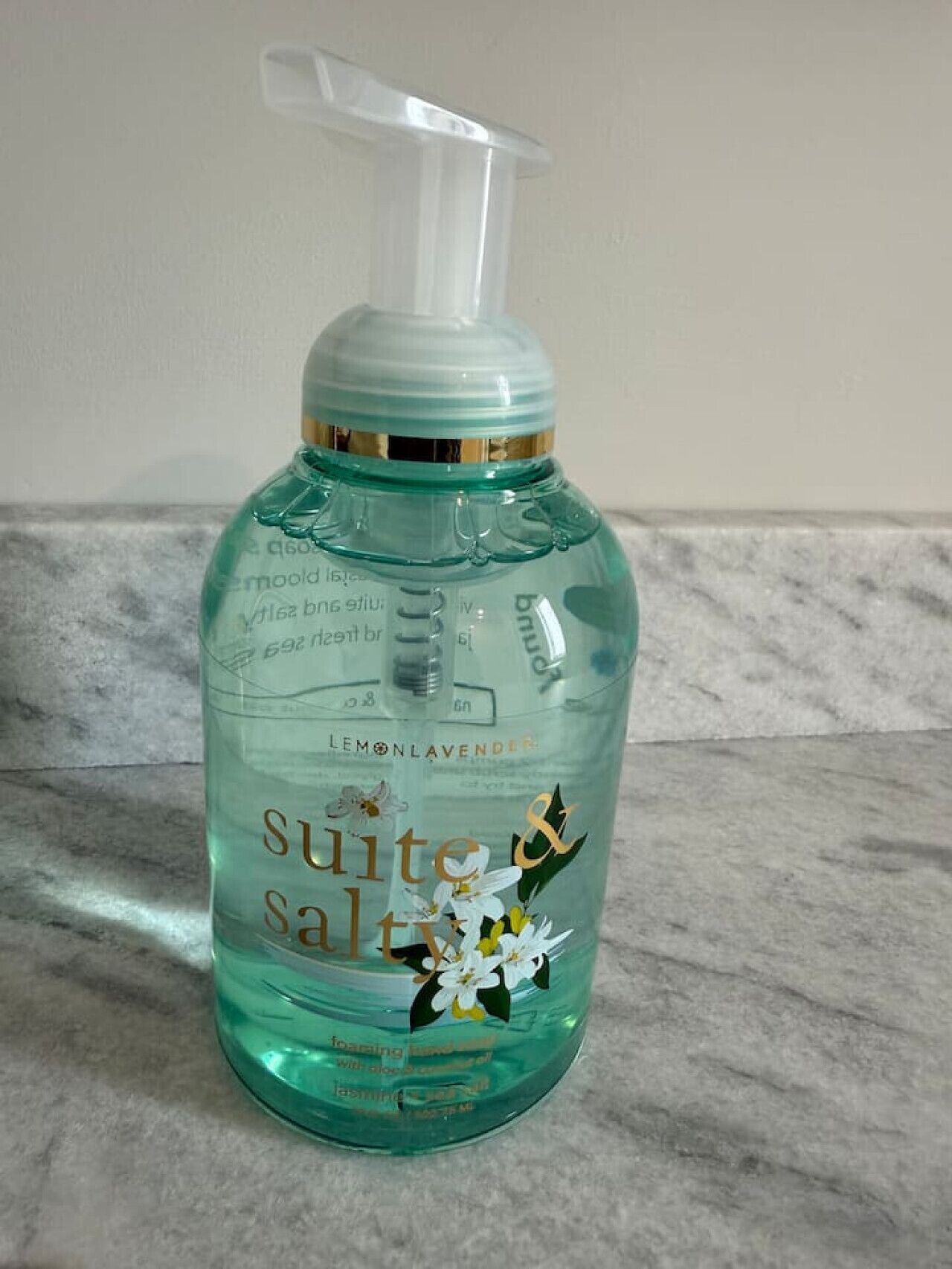 Un flacon de savon liquide pour les mains de la marque « Suite Salt », doté d’un distributeur à pompe, posé sur une surface en marbre.