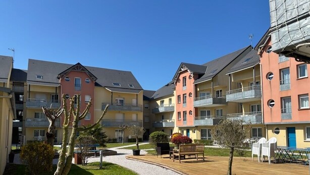 En bostadsbyggnad med flera balkonger, en stenlagd innergård och utomhusmöbler.