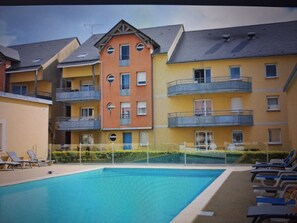 Un immeuble à plusieurs étages doté de balcons, d’une piscine et de chaises longues.