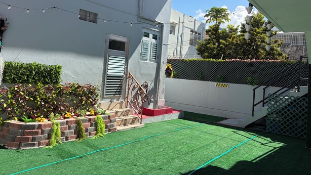 A residential building with a green artificial turf patio, a brick planter with plants, and a staircase with a metal railing. - Charming 1-bedroom Apartment in San Juan, Puerto Rico (San Juan)