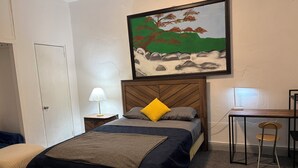 A bedroom with a bed, a nightstand, a desk, a chair, and a painting on the wall. - Charming 1-bedroom Apartment in San Juan, Puerto Rico (San Juan)