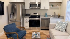 A modern kitchen with stainless steel appliances, white cabinets, and a dining area with a wooden table and blue chairs. - Beautiful 2-Bedroom Apartment 3 Minute Walk From The Beach! (Myrtle Beach)