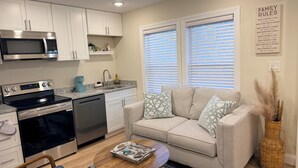 A modern kitchen with stainless steel appliances, a dining area with a sofa and coffee table, and a living room with a large window and a decorative wall piece. - Beautiful 2-Bedroom Apartment 3 Minute Walk From The Beach! (Myrtle Beach)