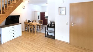 Un espacio habitable compacto con una escalera de madera, un comedor con mesa y sillas, una kitchenette y una puerta.
