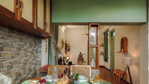 A dining area with a stone wall, wooden table, and green ceiling. - Bir Downtown 2BHK - Landing Site 5 Mins (Baijnath)