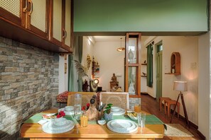 A dining area with a stone wall, wooden table, and green ceiling. - Bir Downtown 2BHK - Landing Site 5 Mins (Baijnath)