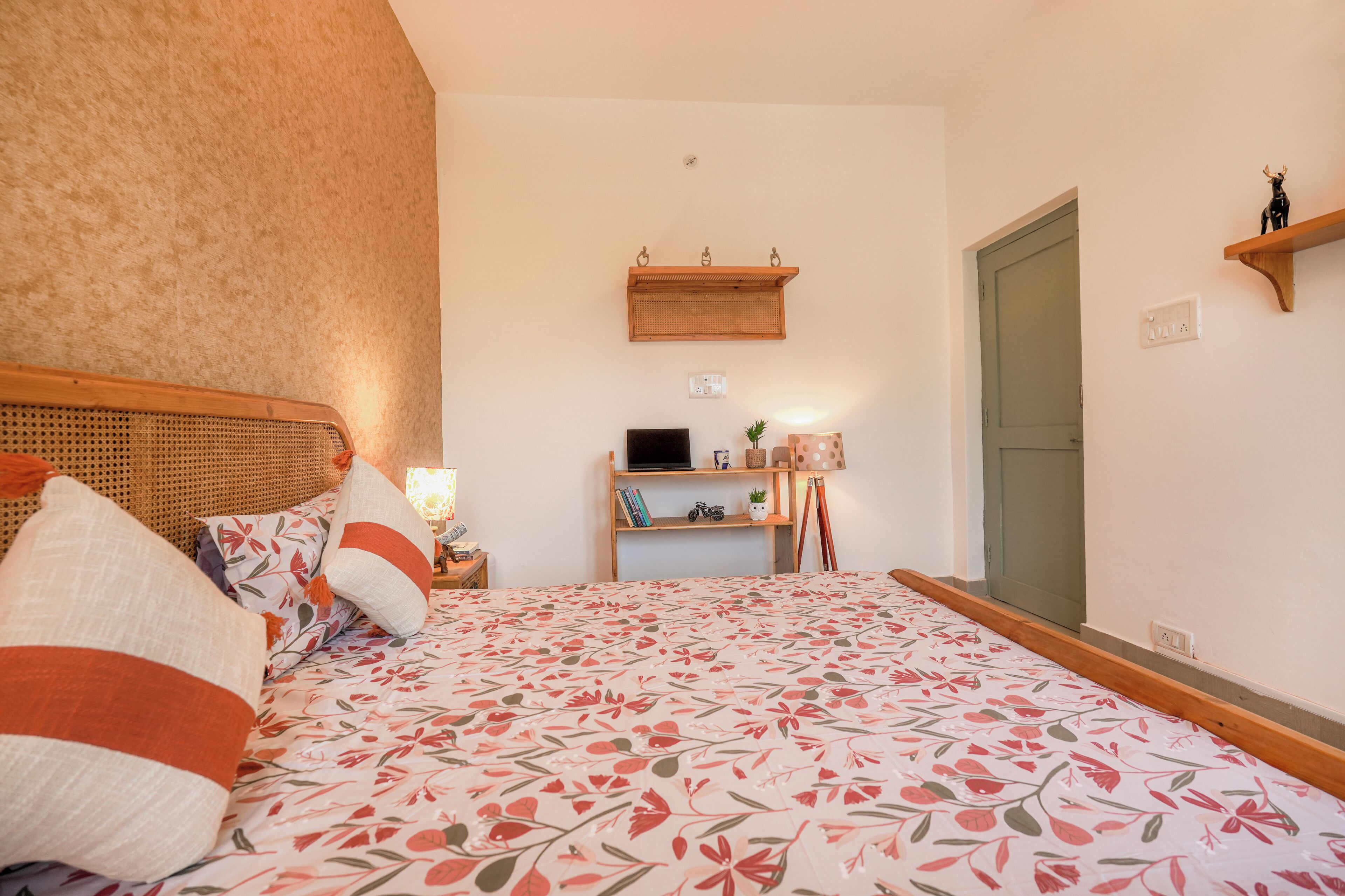 Un dormitorio con cama, cabecera de madera, estante con libros y una planta, y una puerta.