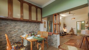 A dining area with a stone wall, wooden cabinets, and a dining table set with chairs. - Bir Downtown 2BHK - Landing Site 5 Mins (Baijnath)