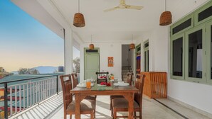 A balcony with a dining table set for four, surrounded by wicker pendant lights, a ceiling fan, and a view of a cityscape. - Bir Downtown 2BHK - Landing Site 5 Mins (Baijnath)