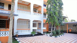 A building with a checkered tile courtyard, white balconies with orange trim, and a tree in the center. - Ristash Green Resort Mtwapa (Mtwapa)