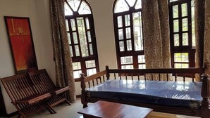 A room with a wooden bench, a small table, and two large windows with curtains. - Ristash Green Resort Mtwapa (Mtwapa)