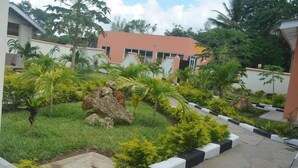 A landscaped courtyard with palm trees, a rock feature, and a building with a red roof. - Ristash Green Resort Mtwapa (Mtwapa)