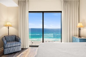 Ein Schlafzimmer mit einem großen Fenster und Meerblick. Es gibt ein Bett, einen Sessel und zwei Lampen.