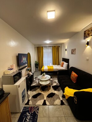 Ein gemütlicher Wohnbereich mit Bett, Sofa, Fernseher, Mikrowelle und einer kleinen Essecke.