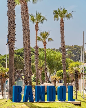 A sign with the word "BANDOL" in large blue letters, surrounded by palm trees and greenery.