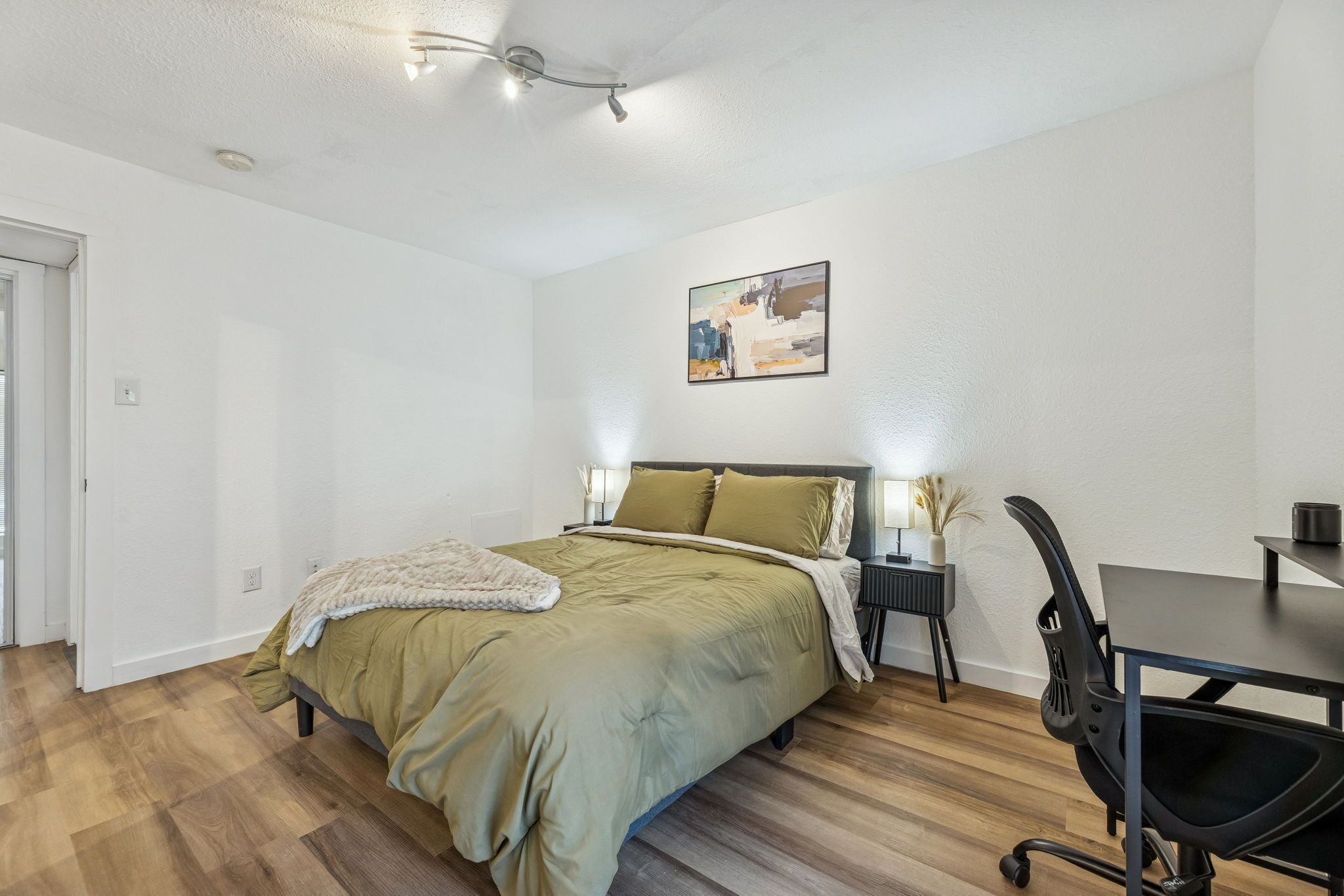 A bedroom with a bed, bedside tables, a desk, and a chair.