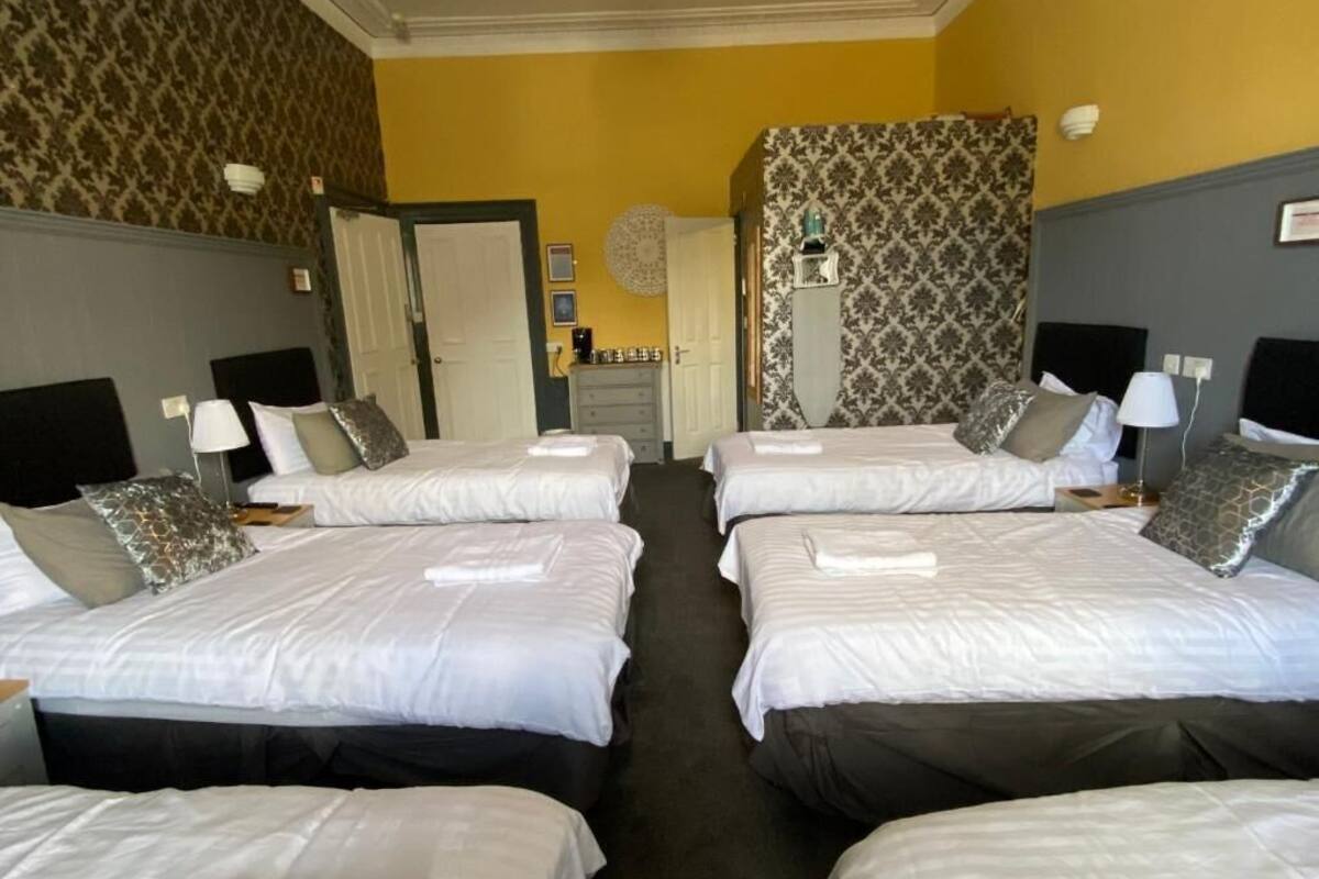 Habitación de hotel con cuatro camas dispuestas en fila, un armario, un espejo y un papel tapiz estampado.
