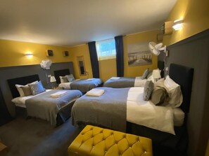 Una habitació d'hotel amb tres llits, un otomà groc i un quadre al mur.