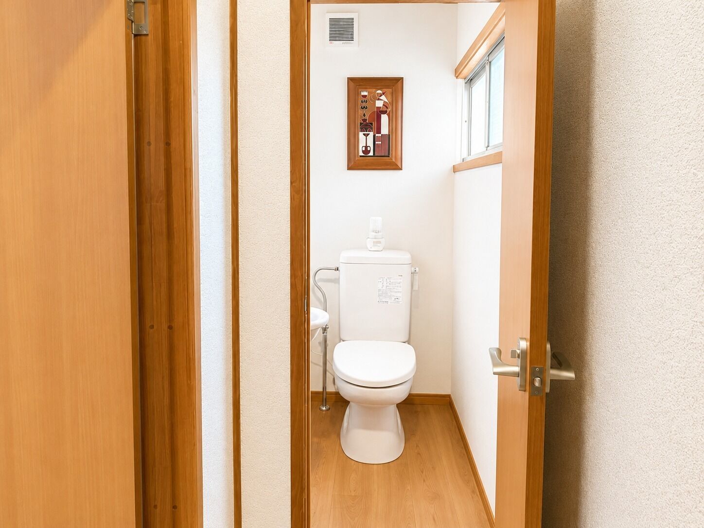 Un bagno con il water, una piccola finestra e un quadro appeso al muro.