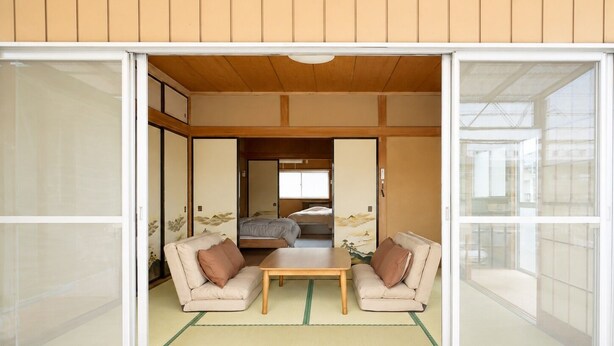 A traditional Japanese room with tatami flooring, a low table, two sofas, and sliding doors.