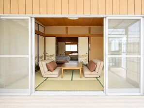 A traditional Japanese room with tatami flooring, a low table, two sofas, and sliding doors. - The Old Futon Shop HU1 (Midori)