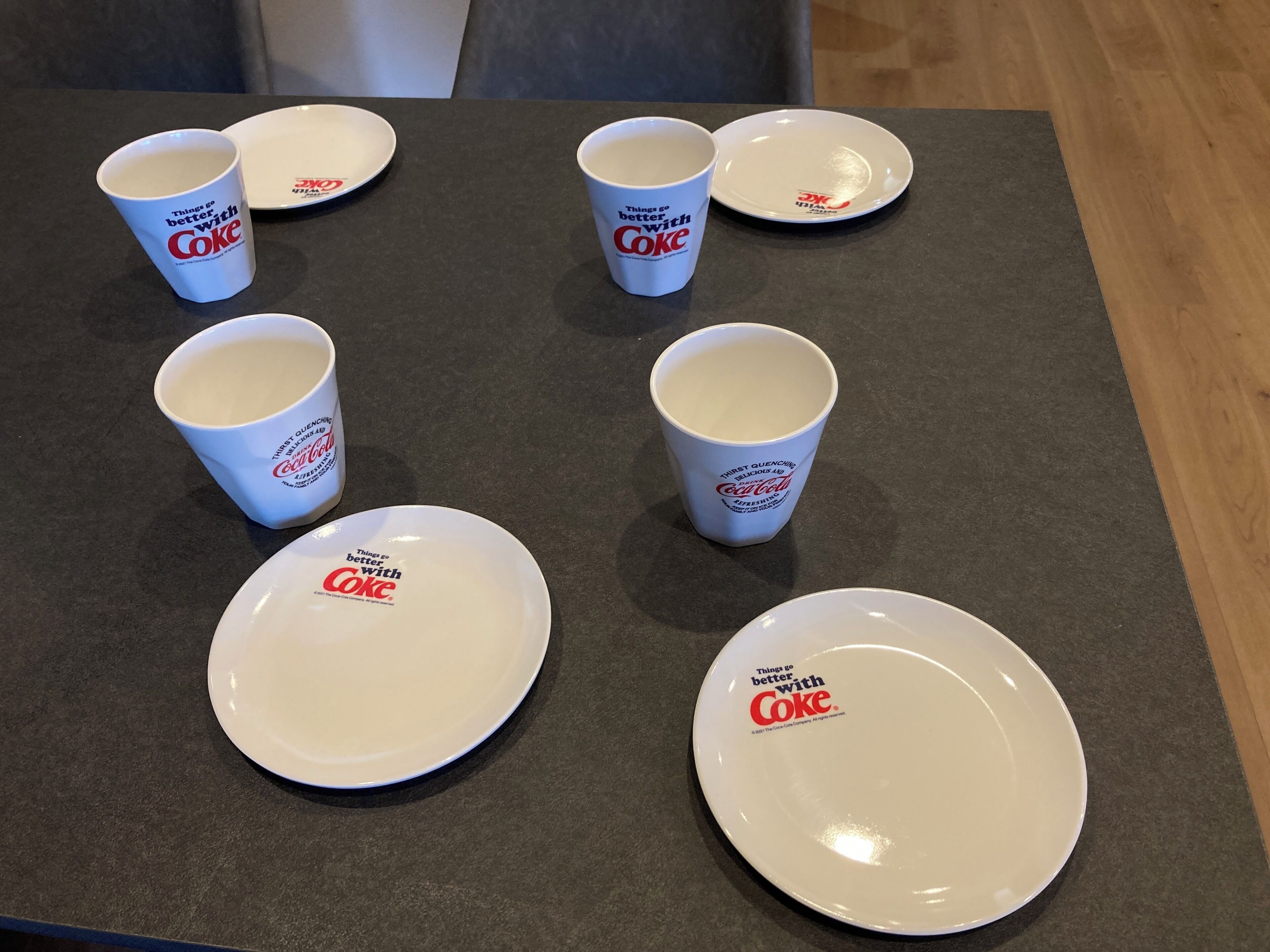 Une table avec six assiettes blanches et six tasses blanches, toutes ornées de l’inscription « Tout est meilleur avec Coca-Cola ».