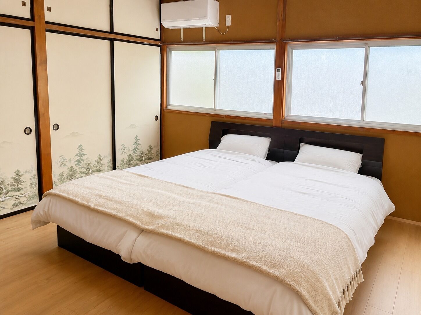A bedroom with a bed, wooden floor, sliding doors with artwork, and a window.