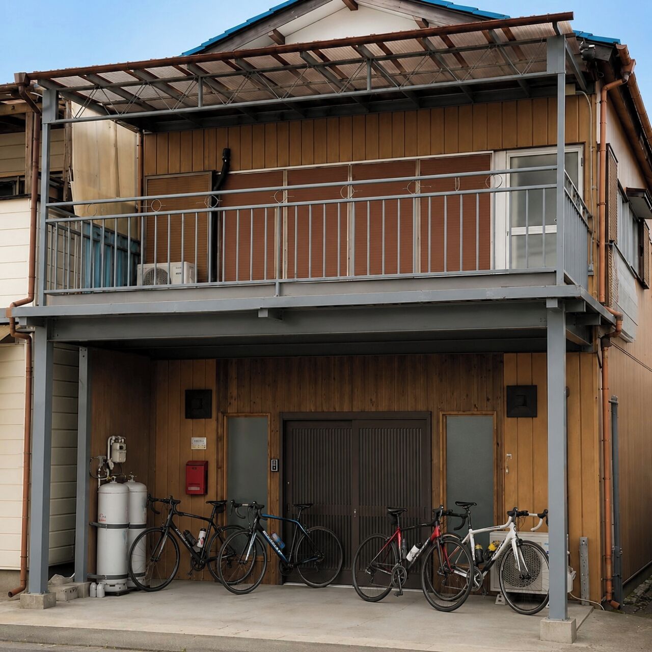Un edificio de dos plantas con un balcón, un portón de garaje y bicicletas estacionadas afuera.