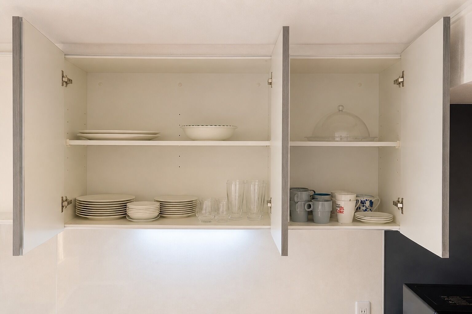 A kitchen with open cabinets, containing plates, bowls, glasses, and mugs.