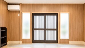 A room with a wooden floor, a black sliding door, and a white air conditioning unit mounted on the wall.