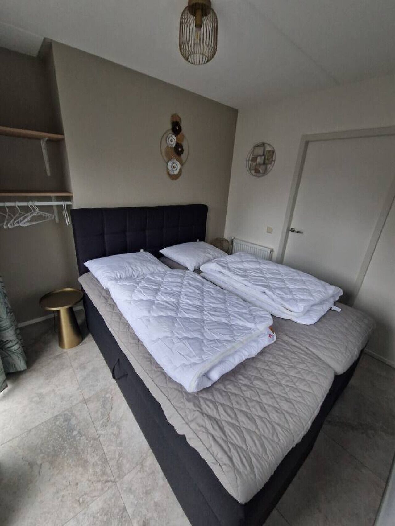 Ein Doppelbett mit gesteppter weißer Bettdecke, einem dunklen Kopfteil und einer runden Wanduhr.