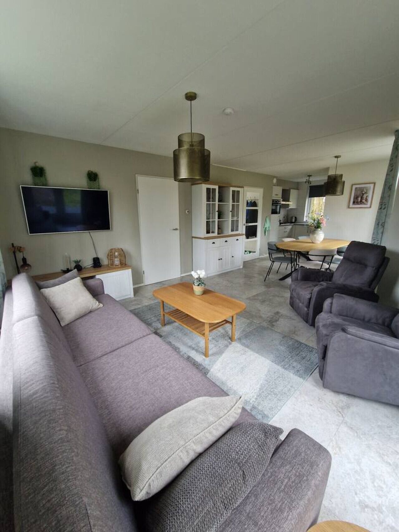 Ein modernes Wohnzimmer mit einer Couch, einem Couchtisch und einem Fernseher. Es gibt einen Essbereich mit Tisch und Stühlen.