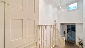 Eine Treppe mit weißen Balustraden führt zu einer zweiten Etage, darüber ein kleines Oberlicht und Blick in einen Küchenbereich.