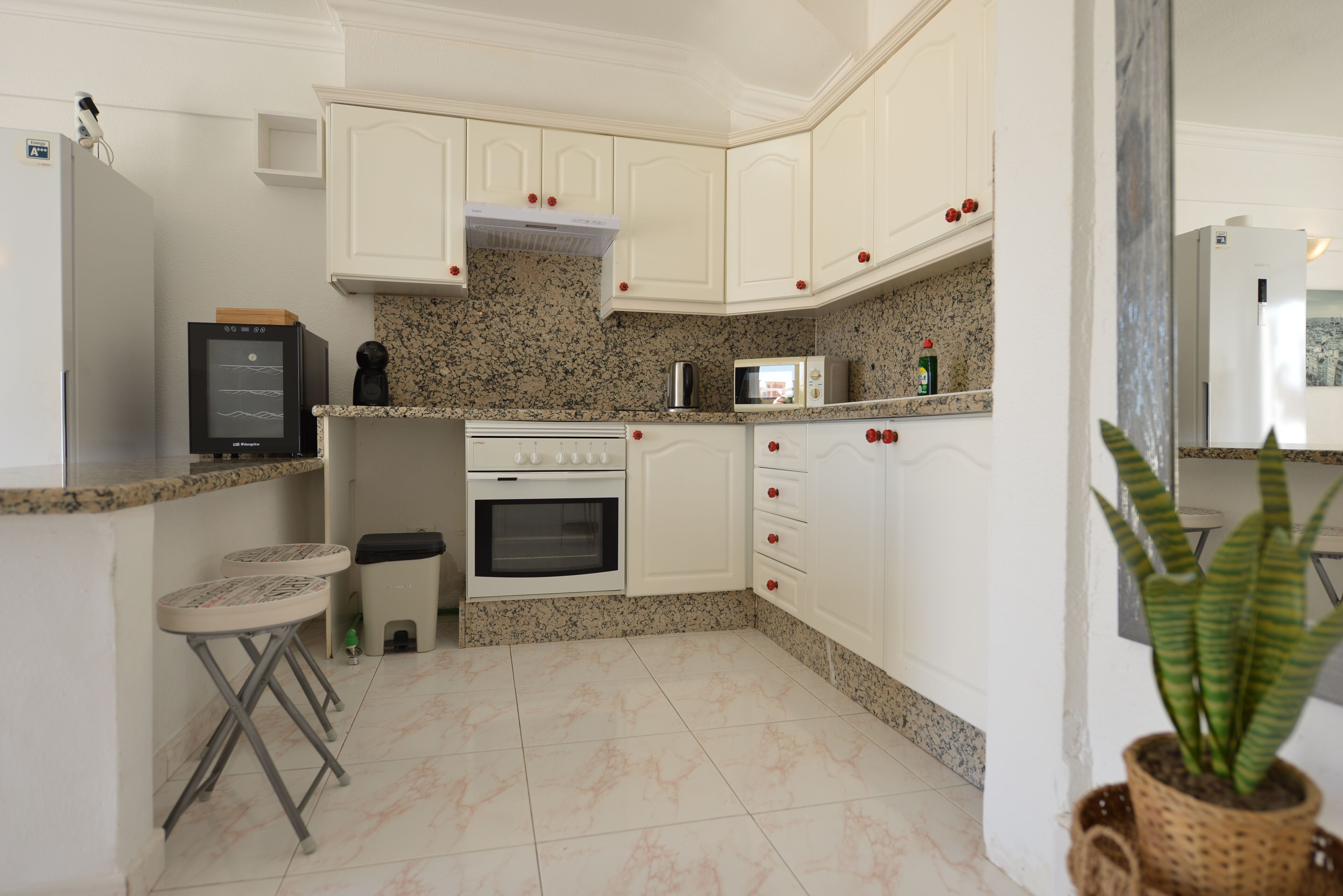 Una cocina con armarios blancos, microondas, estufa y un cubo de basura.