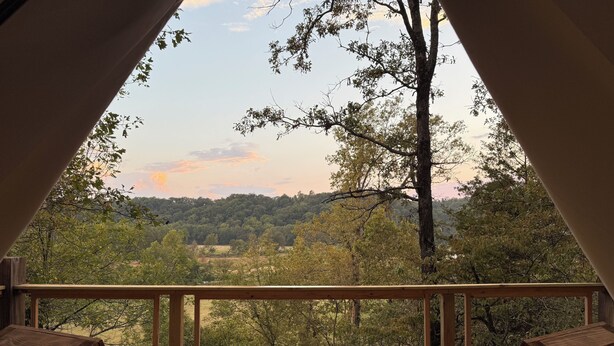 A wooden deck with two chairs and a table, overlooking a forested landscape with trees and a hill in the distance. - Secluded and romantic:  The perfect glamping getaway guests are loving! (Siloam Springs)