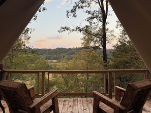 A wooden deck with two chairs and a table, overlooking a forested landscape with trees and a hill in the distance. - Secluded and romantic:  The perfect glamping getaway guests are loving! (Siloam Springs)