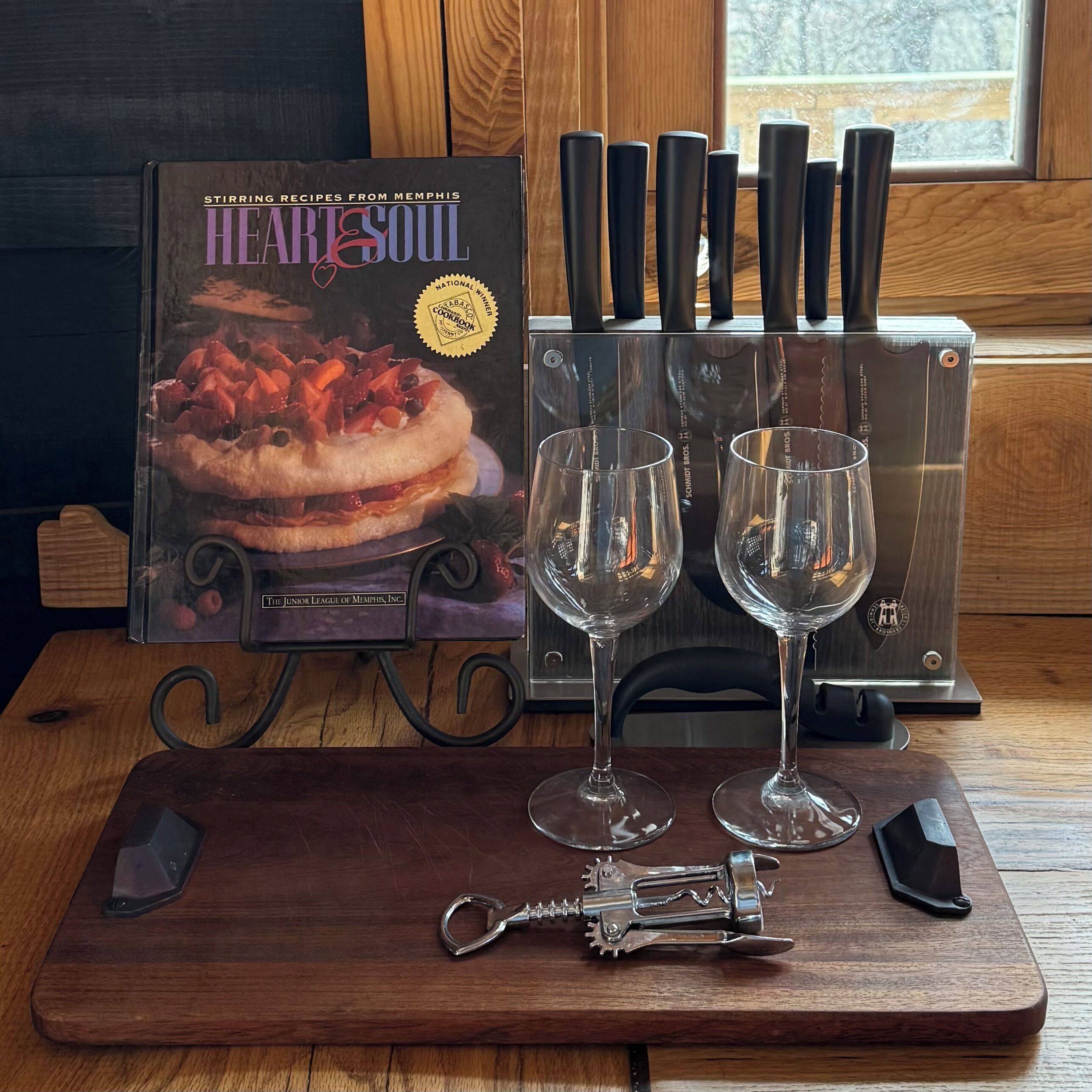 Ein Kochbuch mit dem Titel „HEARTSOUL“ auf einem Holztisch, zusammen mit zwei Weingläsern und einem Korkenzieher.