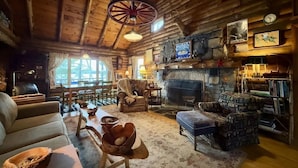 Interior acogedor de una cabaña de troncos con chimenea, muebles de madera y decoración rústica.