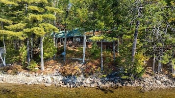 A cabin surrounded by trees and a rocky shoreline.
