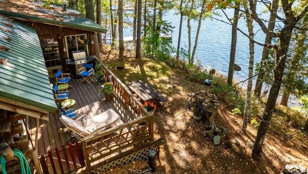 Una cabaña con terraza, asientos exteriores y vistas al lago.